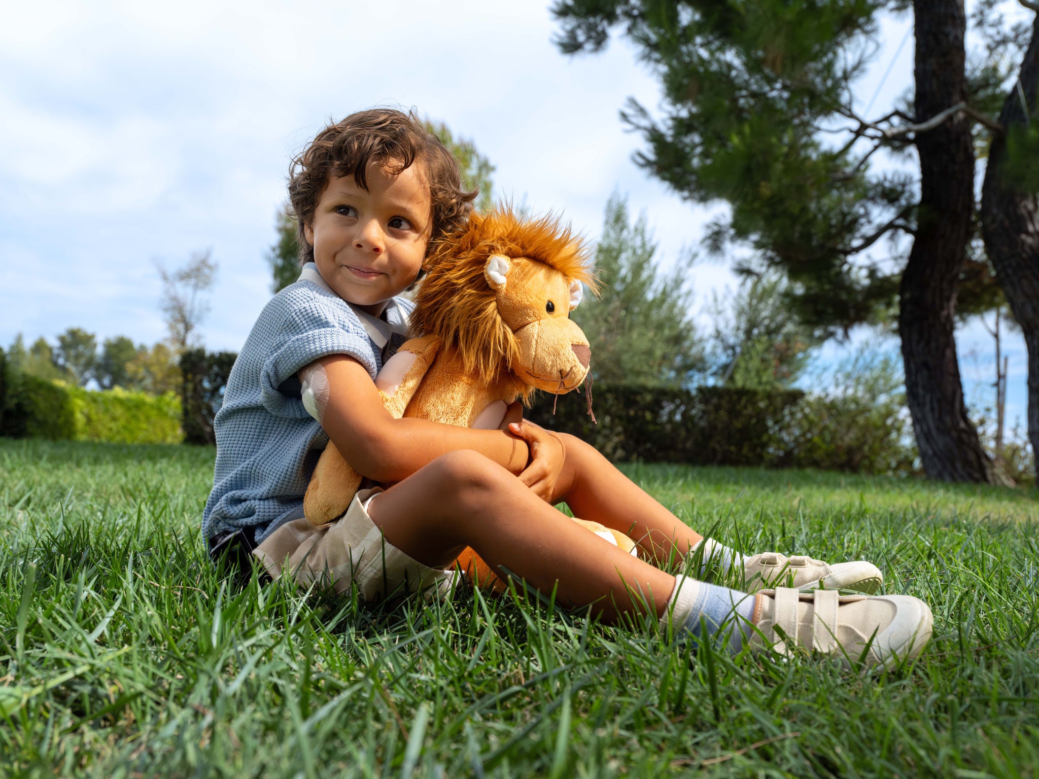 Young child sitting on grass with guardian sensor on his arm hugging a stuffed lion toy.